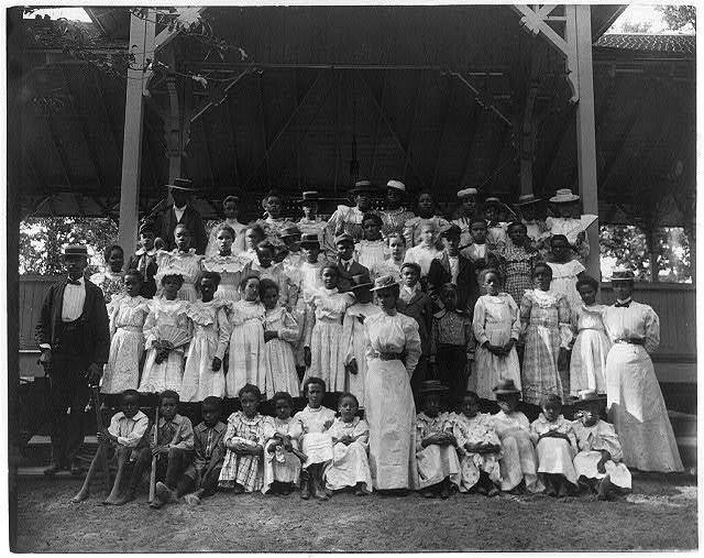 Black children in pavilion with a few adults circa 1899
