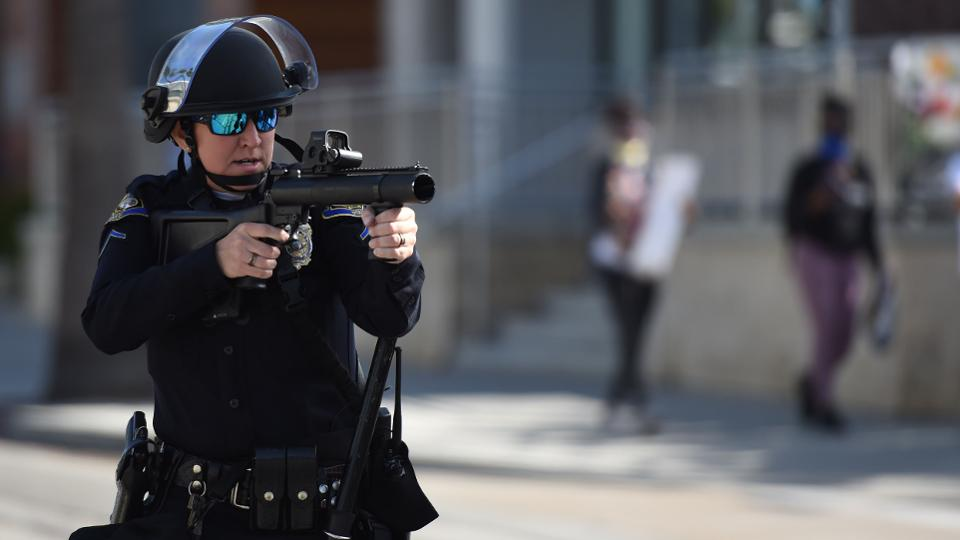 Cop in riot gear pointing weapon at Black Lives Matter ralley