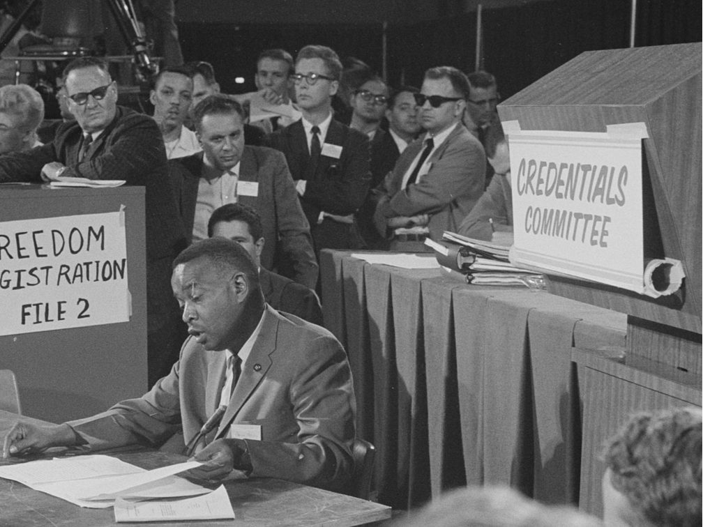 Aaron Henry reading from a document while seated before the credentials committee in 1964