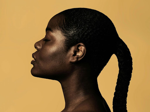 braided woman taking photo beside yellow painted wall