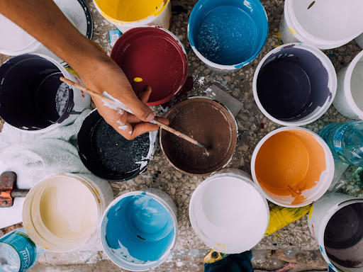 person with a paint brush in hand over open paint buckets