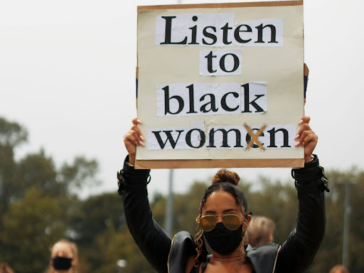 black woman holding up a sign saying listen to black women
