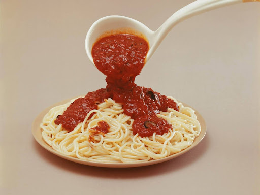 a spoon pouring sauce onto a plate of spaghetti