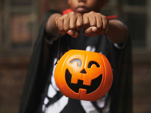 young child wearing modern halloween costume holding a plastic pumpkin decoration