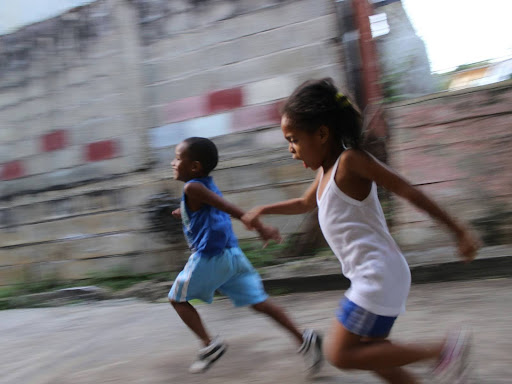 girl and boy running beside gray wall