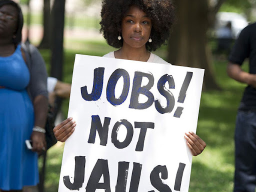 black woman holding a sign saying jobs not jails