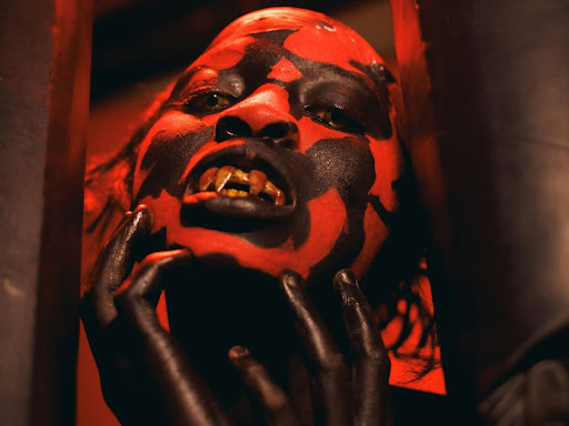a person in a red and black mask holding their hand up to their face