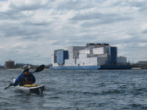 person on a kayak next to the floating boat jail