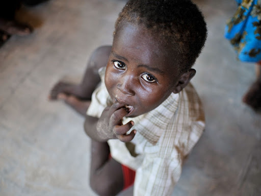 black child sitting down with fingers in mouth