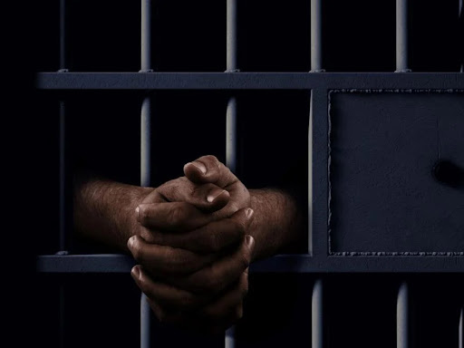 person with hands clasped through prison bars