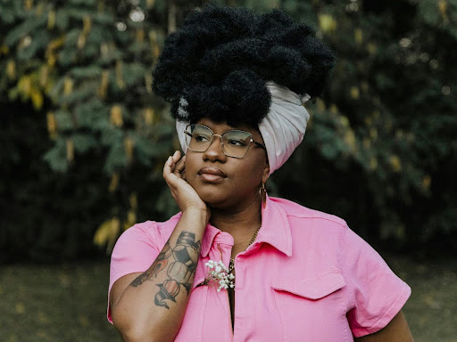 black woman earing a pink shirt and a black and white headwrap with hand on cheek