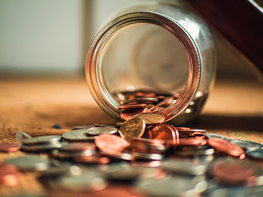 jar of money on a table with coins spilling out