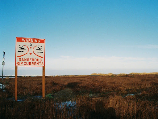 a red and white sign that shows dangers of rip tides