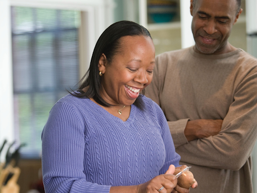 black man and black woman standing close together smiling down at a vegetable the black woman is holding