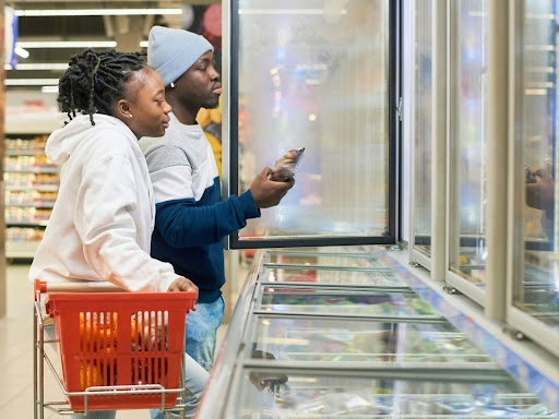 young couple with shopping cart choosing frozen food products in a supermarket