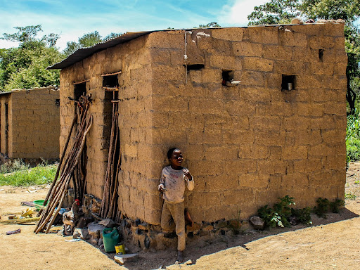 little black child leaning against a clay house