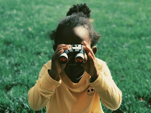 young. black girl on grass field holding binoculars