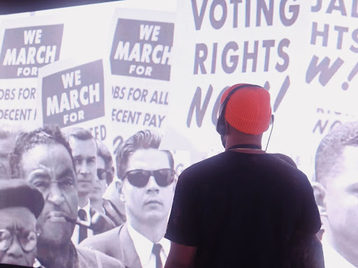 person standing in front of picture of people holding voting rights protest signs