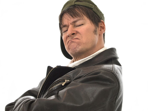 white person crossing their arms and scrunching their face up with a sideways cap on