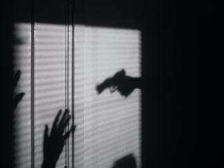 Shadow of gun pointing to person with hands up