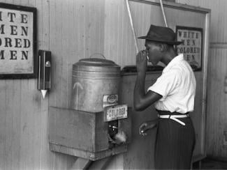 black man drinking from a fountained labeled "colored"