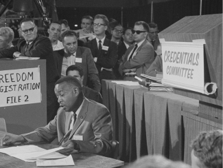 Aaron Henry reading from a document while seated before the credentials committee in 1964