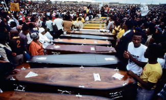 Caskets lined up with crowd of people surrounding them
