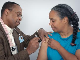 Black doctor administering a vaccination shot to Black patient 