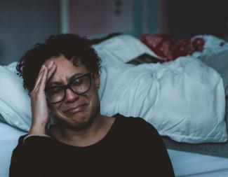 Woman crying while sitting in front of a bed 