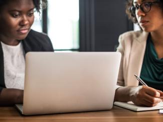 two black women sitting in front of a laptop