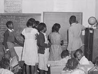 teacher explaining decimals to seventh grade students in a one room schoolhouse