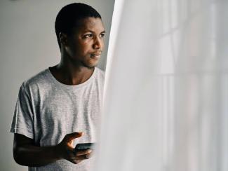 Man holding cell phone looking out of a window