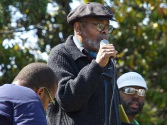 amiri baraka standing with a microphone in front of his mouth speaking to a crowd