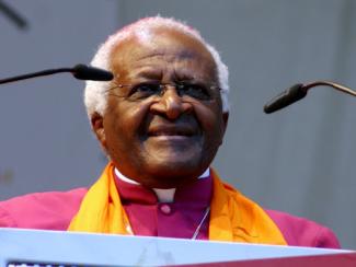 bishop desmond tutu speaking at a podium in front of microphones to a crowd