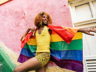 person in a yellow shirt and colorful skirt holding a pride flag
