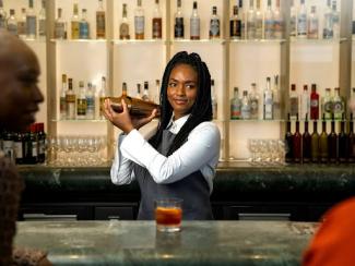 a black woman standing at a bar pouring a drink