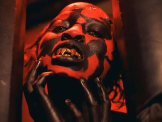 a person in a red and black mask holding their hand up to their face