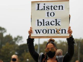 black woman holding up a sign saying listen to black women