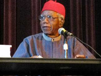 chinua achebe sitting down in front of a microphone at a table