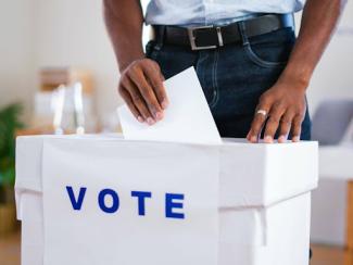 black man putting his ballot in a white box that says vote