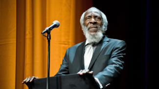 dick gregory standing at a podium speaking in front of a microphone