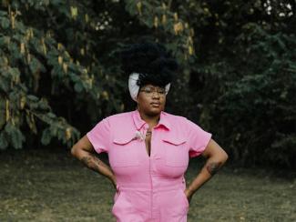 black woman in a pink jumpsuit standing in the grass