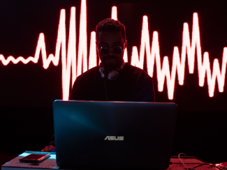 black man in a dj booth with a laptop in front of him