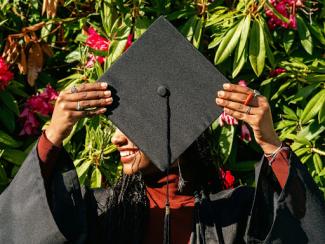 graduate in cap and gown smiles behind mortarboard