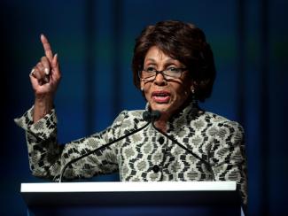 maxine waters in front of a podium with a finger raised