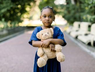 little black girl in style blue dress holding a teddy bear