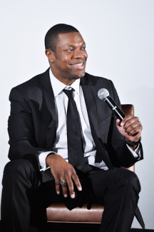 chris tucker with microphone in hand sitting down