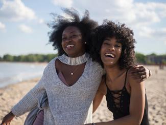 two black women on a beach smiling