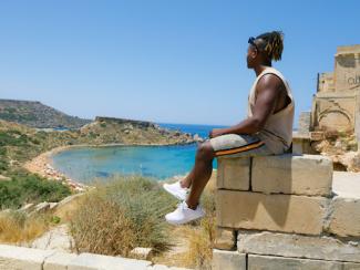 black man sitting on a wall next to the beach