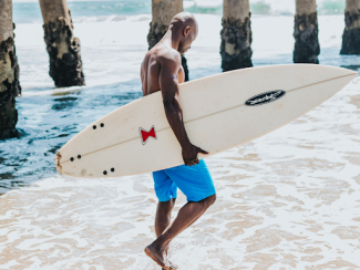 black man holding a surfboard on a beach